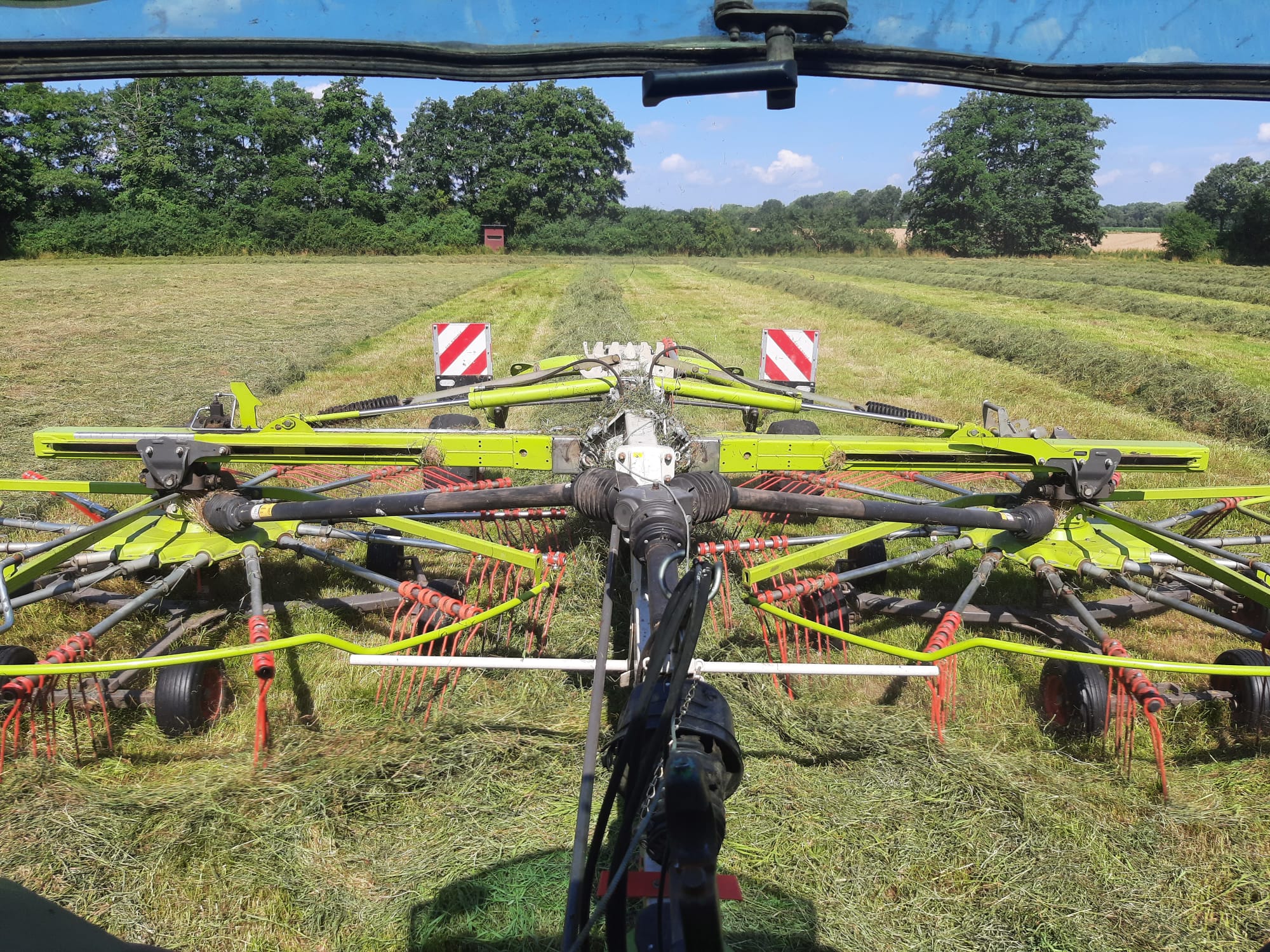 Blick aus Traktor auf Schwader beim Zusammenrechen von frisch gemähtem Gras.