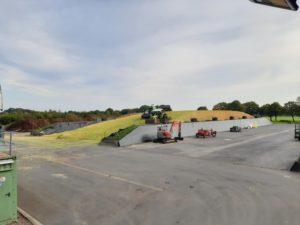 Großer Fahrsilo mit Maissilage, Traktor verdichtet, Lagerplatz mit Maschinen und Kompost.
