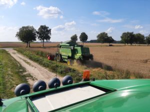 John Deere Mähdrescher erntet Getreide am Feldrand, weiteres Fahrzeug im Vordergrund.