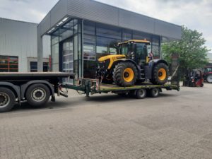 Gelb-schwarzer JCB Fastrac auf Tieflader vor modernem Industriegebäude mit Glasfassade.