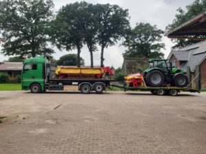 MAN-Sattelzug mit Deutz-Traktor und gelb-rotem Mähwerk auf Bauernhof mit Kopfsteinpflaster.